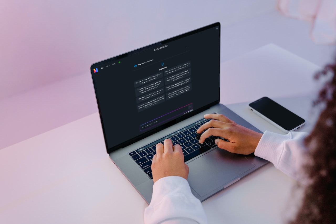 woman typing on a macbook pro on a white desk. the macbook pro screen shows a chatgpt-like interface