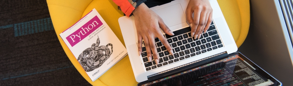 Woman typing on her computer, with a book about Python by her side