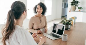 two-women-chatting-smiling-sitting-at-a-table-in-a-professional-environment-leadership-insights-chro-peopleops-team-hr