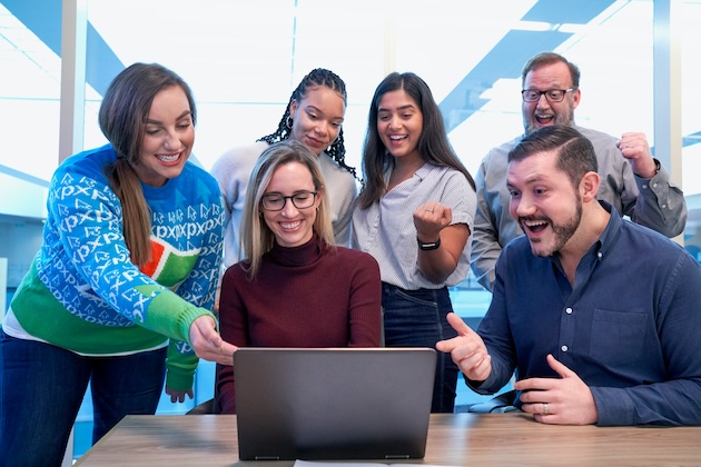 men and women sitting and standing while staring at laptop