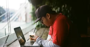 Cultural Sensitivity: man holding phone in with laptop beside cup