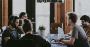 Nearshore Software Development Outsourcing: team of software developers share a large table, collocated work day